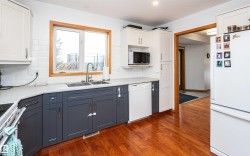 Kitchen featuring two-tone cabinetry, a stainless steel double basin sink with a high-arc faucet, and wood-finish flooring - 