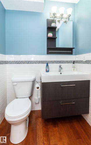 Bathroom featuring a wall-mounted vanity with integrated sink, rectangular mirror with built-in shelving, and brushed nickel light fixture - 5502 60 Avenue, Barrhead, AB - Indoor Photo Showing Bathroom