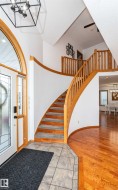 Grand foyer featuring a curved staircase with natural wood banister, a decorative arched transom window, and a geometric pendant light fixture - 