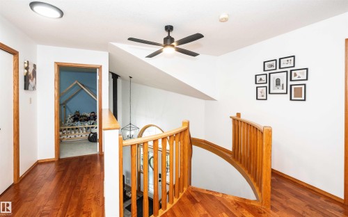Hardwood-finish flooring throughout, featuring a natural wood staircase with curved railing, a contemporary ceiling fan, recessed lighting, and a doorway to an additional room - 5502 60 Avenue, Barrhead, AB - Indoor Photo Showing Other Room