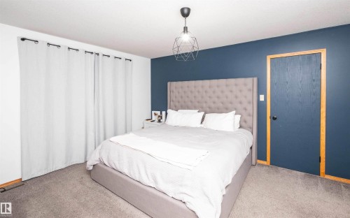 Bedroom featuring plush grey carpeting, a modern geometric pendant light, and a two-tone wall treatment with a deep blue accent wall - 5502 60 Avenue, Barrhead, AB - Indoor Photo Showing Bedroom