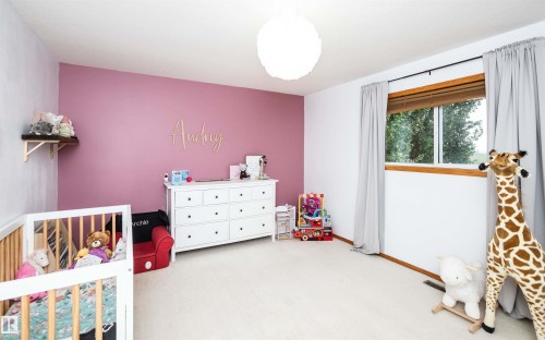 Room featuring a partial accent wall with a light pink finish, light-colored carpet, a window with wood trim, and a white ceiling light fixture - 5502 60 Avenue, Barrhead, AB - Indoor Photo Showing Bedroom