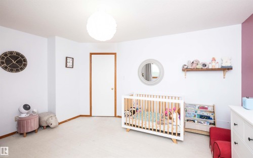 Carpeted room with a white door featuring wood trim, a circular ceiling light fixture, a built-in wall shelf, and a color-blocked accent wall - 5502 60 Avenue, Barrhead, AB - Indoor Photo Showing Bedroom
