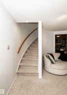 Curved staircase with a light wood handrail, recessed ceiling lighting, and neutral-toned carpeting throughout - 