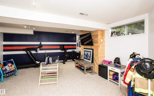 Spacious finished lower level featuring light-colored carpeting, a horizontal window providing natural light, a wood-paneled accent wall, track lighting, and a painted accent wall with white and orange stripes - 5502 60 Avenue, Barrhead, AB - Indoor Photo Showing Other Room