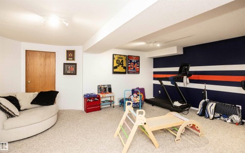 Finished basement space featuring track lighting, light-toned carpeting, a wood-finish door, and a distinctive accent wall with horizontal striping - 5502 60 Avenue, Barrhead, AB - Indoor