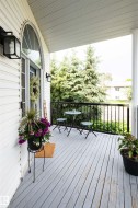 Covered front porch featuring white siding and a light-colored wood-finish deck - 