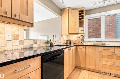 Maple cabinetry with integrated wine rack, black countertops, tile backsplash, stainless steel sink with gooseneck faucet, and track lighting - 14307 50 Avenue Nw, Edmonton, AB 