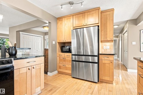 Kitchen featuring wood-finish cabinetry, stainless steel refrigerator, black granite countertops, and wood-finish flooring - 14307 50 Avenue Nw, Edmonton, AB 