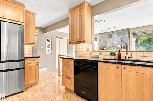Kitchen featuring wood-finish cabinetry, black countertops, a stainless steel refrigerator, and a tile backsplash - 14307 50 Avenue Nw, Edmonton, AB 