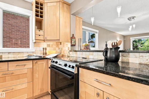 Maple cabinetry with brushed nickel hardware, black stone countertops, tile backsplash, built-in wall oven, and pendant lighting - 14307 50 Avenue Nw, Edmonton, AB 
