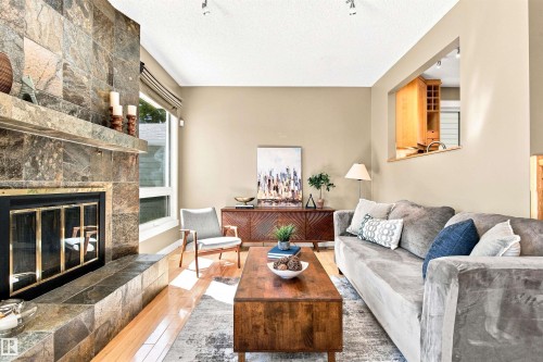 Stone-clad fireplace with hearth, wood-finish flooring, recessed lighting, and a pass-through window with built-in cabinetry - 14307 50 Avenue Nw, Edmonton, AB 