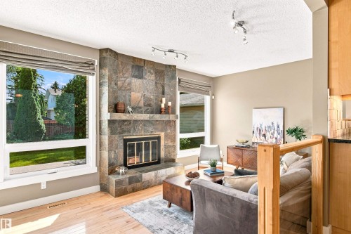 Stone-clad fireplace with a hearth and mantel, large windows with blinds, light wood-finish flooring, and track lighting - 14307 50 Avenue Nw, Edmonton, AB 
