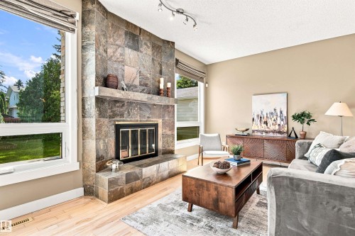 Living area featuring a stone-clad fireplace, light wood-finish flooring, track lighting, and large windows - 14307 50 Avenue Nw, Edmonton, AB 