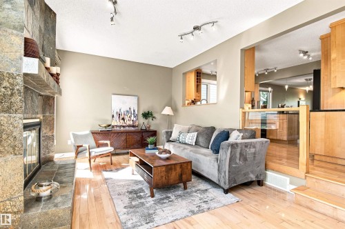 Stone-clad fireplace with hearth, wood-finish flooring, track lighting, and a partial cut-out wall feature - 14307 50 Avenue Nw, Edmonton, AB 