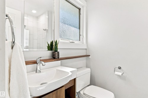 Rectangular vessel sink with chrome faucet, wood-finish vanity, and a clear glass wall mirror - 14307 50 Avenue Nw, Edmonton, AB 