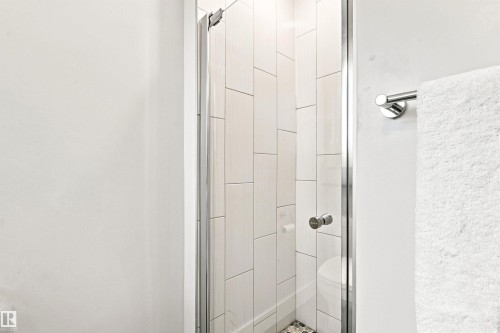 Shower enclosure featuring a clear glass door, white rectangular tile surround, pebble tile flooring, and polished chrome hardware - 14307 50 Avenue Nw, Edmonton, AB 