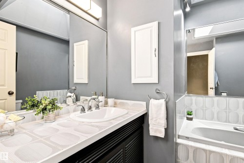 Bathroom featuring a built-in tub, extensive mirrored wall, vanity with an integrated sink, wall-mounted medicine cabinet, and decorative tiled surfaces - 14307 50 Avenue Nw, Edmonton, AB 