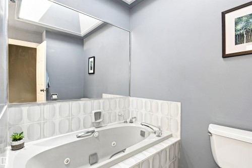 Built-in jetted tub with chrome fixtures, tiled surround featuring a geometric pattern, and a large wall-mounted mirror - 14307 50 Avenue Nw, Edmonton, AB 