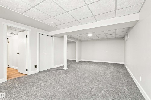 Expansive room featuring plush carpeting, crisp white walls, and a suspended acoustic tile ceiling - 14307 50 Avenue Nw, Edmonton, AB 