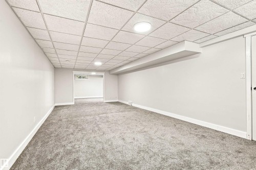 Spacious room featuring neutral carpeting, light-colored walls, and a dropped ceiling with integrated circular lighting fixtures - 14307 50 Avenue Nw, Edmonton, AB 