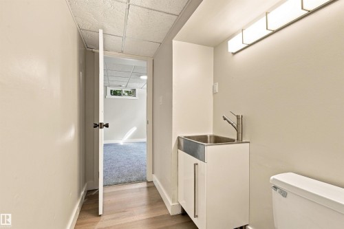 White vanity with integrated stainless steel sink, contemporary wall-mounted light fixture, and light wood-finish flooring - 14307 50 Avenue Nw, Edmonton, AB 
