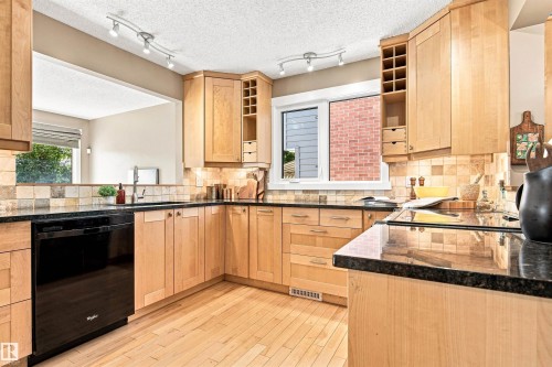 Wood-finish flooring, black appliances, granite countertops, tile backsplash, and light wood cabinetry - 14307 50 Avenue Nw, Edmonton, AB 