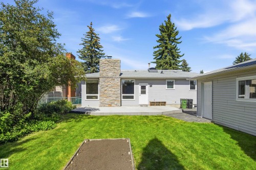Expansive backyard featuring a manicured lawn, stone-clad chimney, and a concrete patio - 14307 50 Avenue Nw, Edmonton, AB 