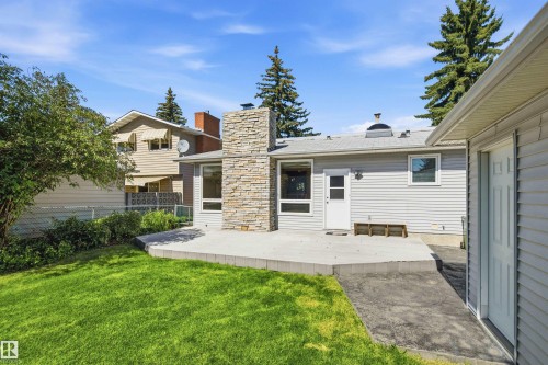 Expansive green lawn with a large concrete patio, stone-clad chimney, and horizontal siding - 14307 50 Avenue Nw, Edmonton, AB 