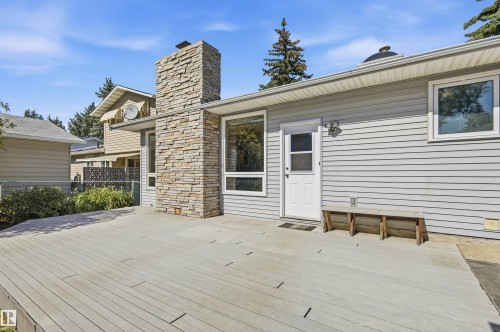 Expansive rear deck, stone-clad chimney, light-toned siding, exterior light fixture, and multiple windows - 14307 50 Avenue Nw, Edmonton, AB 
