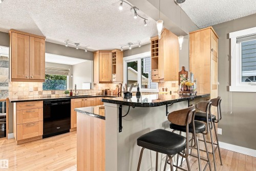 Full kitchen featuring light wood cabinetry, black countertops, a tile backsplash, and a breakfast bar with pendant lighting - 14307 50 Avenue Nw, Edmonton, AB 