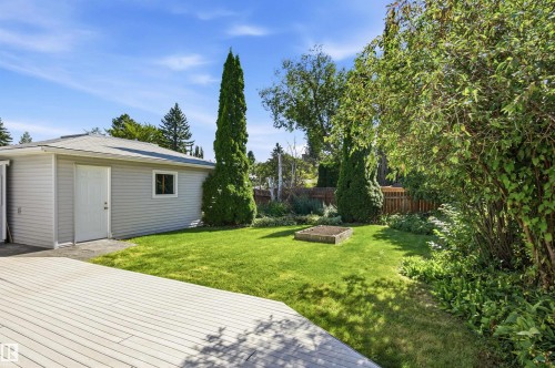 Spacious backyard featuring a large composite deck, manicured lawn, detached accessory building, mature trees, and privacy fencing - 14307 50 Avenue Nw, Edmonton, AB 
