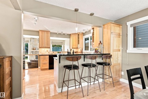 Kitchen featuring wood-finish flooring, natural wood cabinetry, a dark-toned countertop island with pendant lighting, and an integrated black appliance - 14307 50 Avenue Nw, Edmonton, AB 