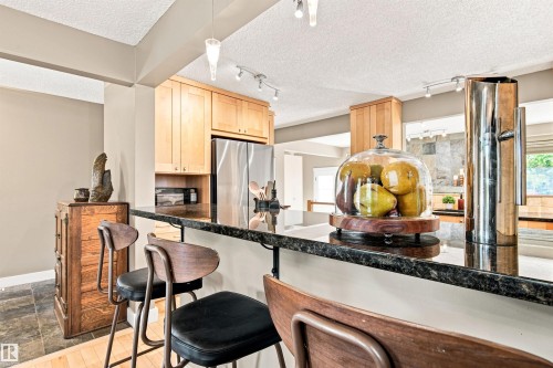 Kitchen featuring a breakfast bar with dark countertops, wood cabinetry, and stainless steel appliances - 14307 50 Avenue Nw, Edmonton, AB 