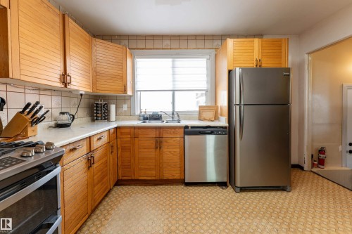 Kitchen featuring light wood cabinetry, white countertops, tile backsplash, stainless steel refrigerator, and stainless steel dishwasher - 14906 76 Avenue Nw, Edmonton, AB 