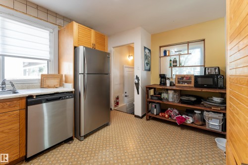 Kitchen featuring wood cabinets, a stainless steel refrigerator, a stainless steel dishwasher, a single basin sink, and patterned flooring - 14906 76 Avenue Nw, Edmonton, AB 