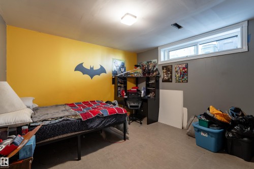 Finished Basement Bedroom with Vibrant Yellow Accent Wall, Built-In Black Shelving Unit with Display Space, Recessed Ceiling Lighting, Carpeted Flooring, and Transom Windows for Natural Light - 14906 76 Avenue Nw, Edmonton, AB 