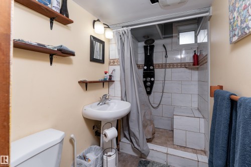 Shower with tiled walls and built-in bench, pedestal sink, wall-mounted lighting, and wood shelving - 14906 76 Avenue Nw, Edmonton, AB 