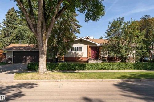 Stucco exterior with a peaked roof, mature front landscaping, attached garage, and a red front entry door - 14906 76 Avenue Nw, Edmonton, AB 