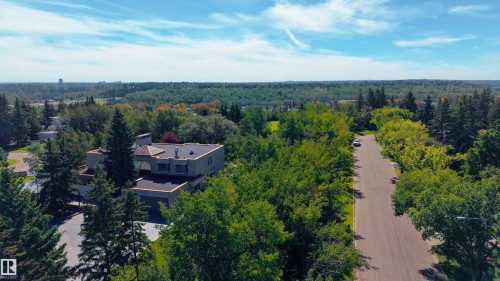 Contemporary flat-roof residence surrounded by mature trees, featuring an attached garage and a paved driveway - 14906 76 Avenue Nw, Edmonton, AB 