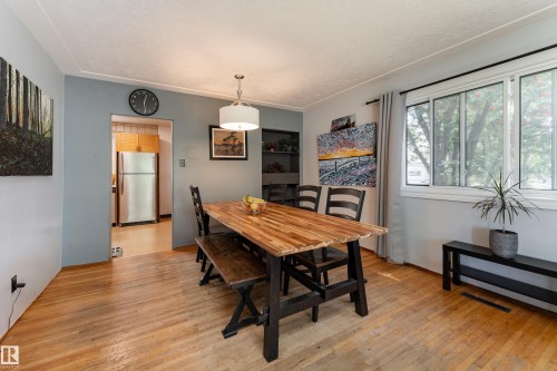 Wood-finish flooring throughout, featuring a drum pendant light fixture, and a large window with white trim - 14906 76 Avenue Nw, Edmonton, AB 