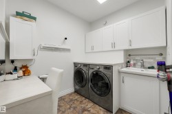 Laundry area featuring tiled flooring, a built-in sink with a stainless steel faucet, and white shaker-style cabinetry with brushed nickel hardware - 