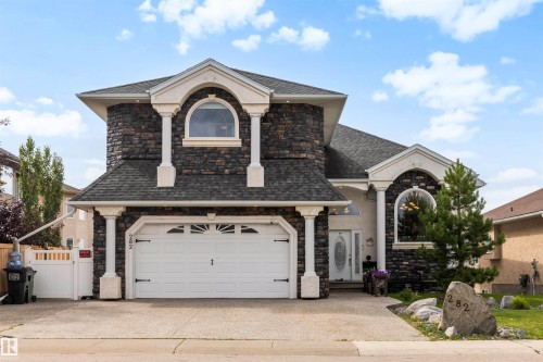 Stone veneer facade with decorative columns, prominent arched windows, dual garage doors, and a double entry door - 282 Ozerna Road Nw, Edmonton, AB 