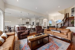 Expansive living area featuring wood-finish flooring, recessed lighting, and a grand staircase with dark wood railings - 