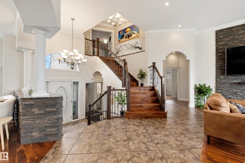 Two-story foyer featuring tile flooring, a wood staircase with wrought iron balusters, and a decorative arched window - 282 Ozerna Road Nw, Edmonton, AB 