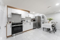 White cabinetry with wood-finish trim, stainless steel appliances, stacked laundry units, and white tile flooring - 