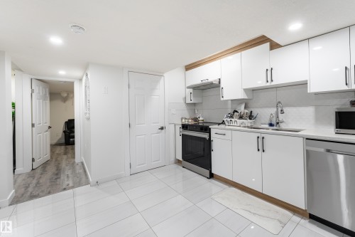 White tiled flooring, white cabinetry with wood-finish accents, stainless steel appliances, and recessed lighting - 13435 101 Street Nw, Edmonton, AB 