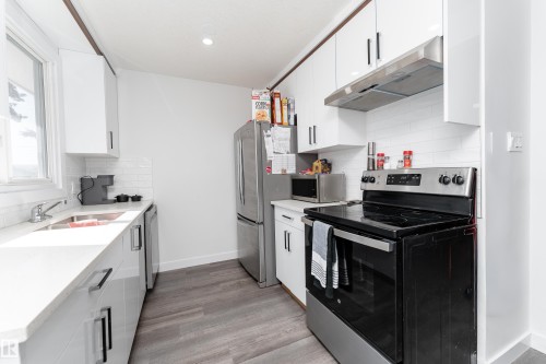 Modern kitchen featuring white cabinetry, a subway tile backsplash, stainless steel appliances, and wood-finish flooring - 13435 101 Street Nw, Edmonton, AB 