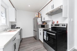 Modern kitchen featuring white cabinetry, a subway tile backsplash, stainless steel appliances, and wood-finish flooring - 