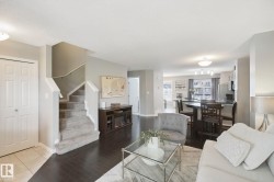 Dark wood-finish flooring, carpeted staircase with white railing, built-in media console, kitchen island with seating, and stainless steel appliances - 